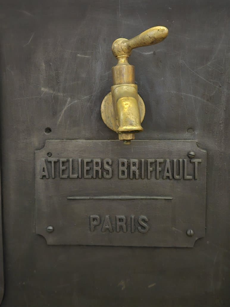 A brass valve handle mounted on a dark cast-iron machine above an embossed builder's plate reading Ateliers Briffault, Paris. The interface is small; the machine is the product.