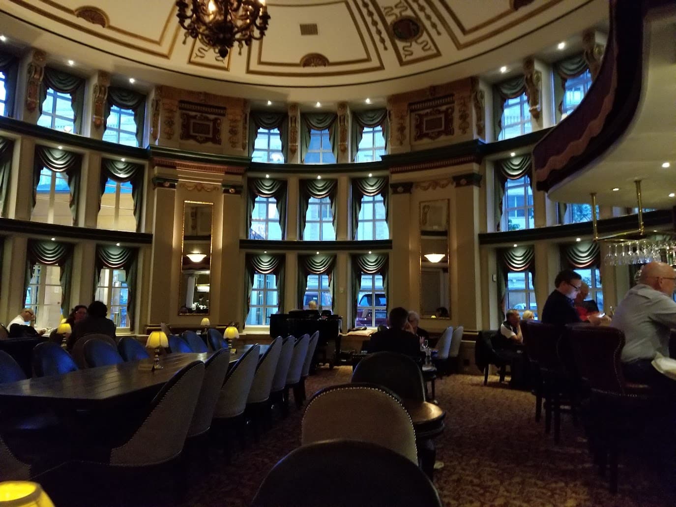 The grand oval bar at the Fort Garry Hotel: chandelier, tall arched windows, leather chairs, dim atmospheric light.